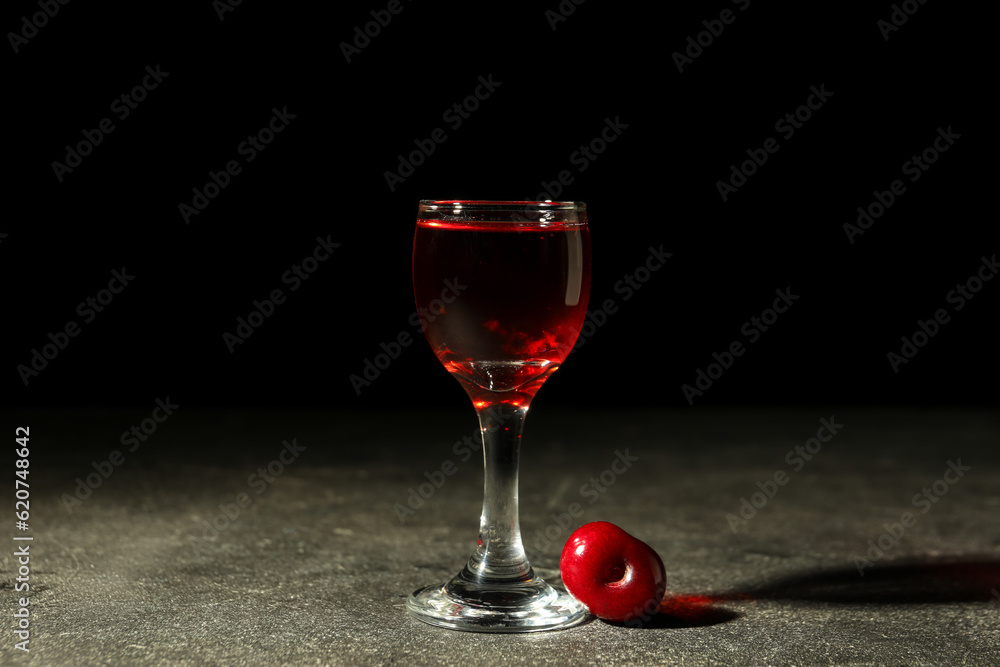 Glass with sweet cherry liqueur on black background