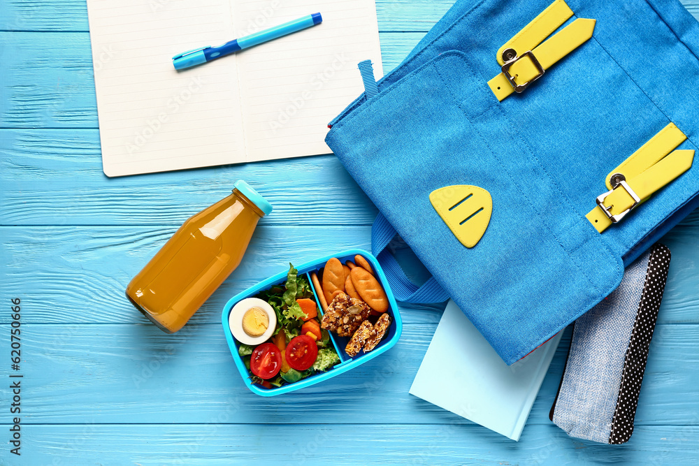 Backpack, stationery and lunchbox with tasty food on blue wooden background