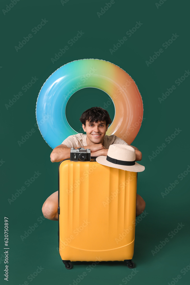 Young man with suitcase, camera and hat on green background