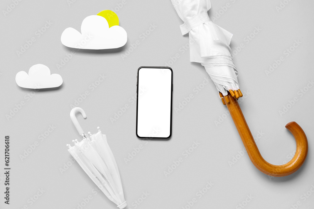 Mobile phone with paper clouds and umbrellas on grey background. Weather forecast concept