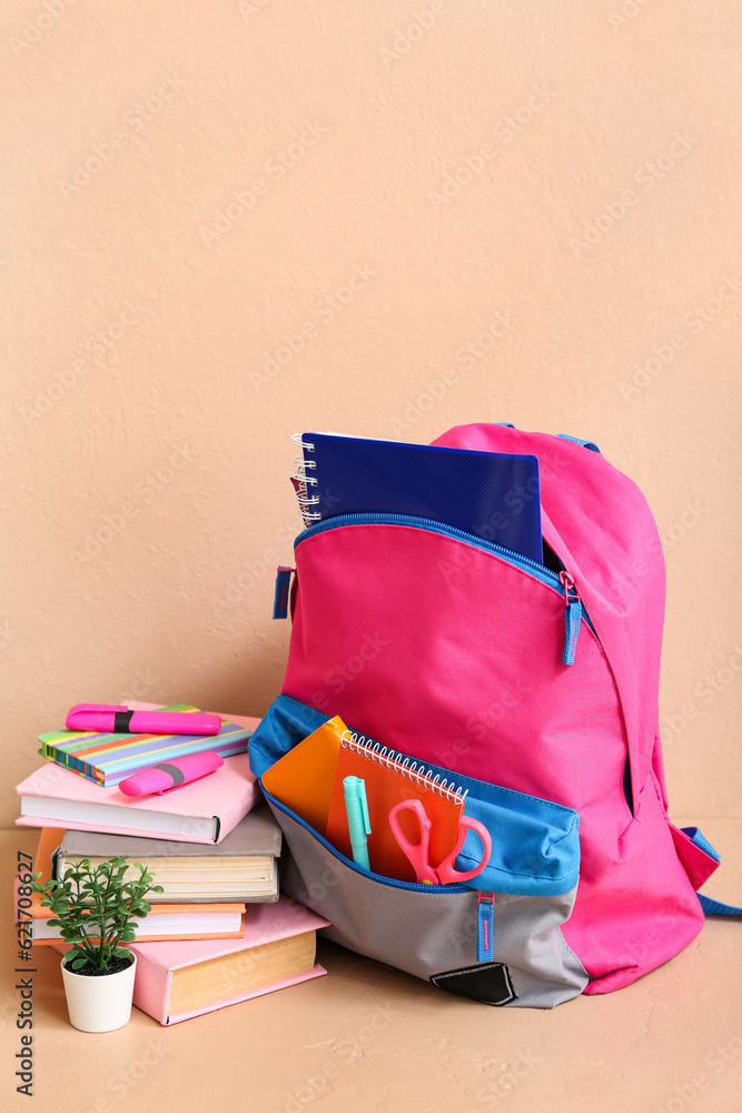 Color school backpack with books, houseplant and markers on table near beige wall