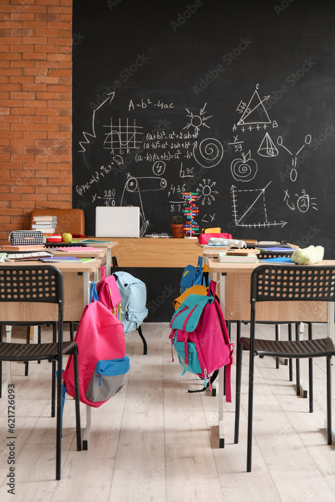 Desks with backpacks and chairs in classroom