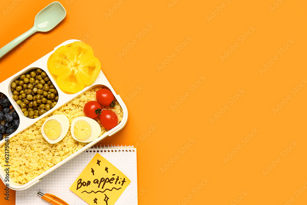 Stationery, tasty food in lunchbox and sticky note with text BON APPETIT on orange background