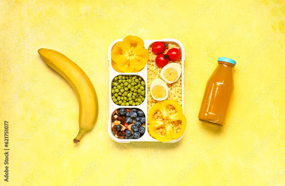 Bottle of juice, banana and lunchbox with tasty food on yellow background
