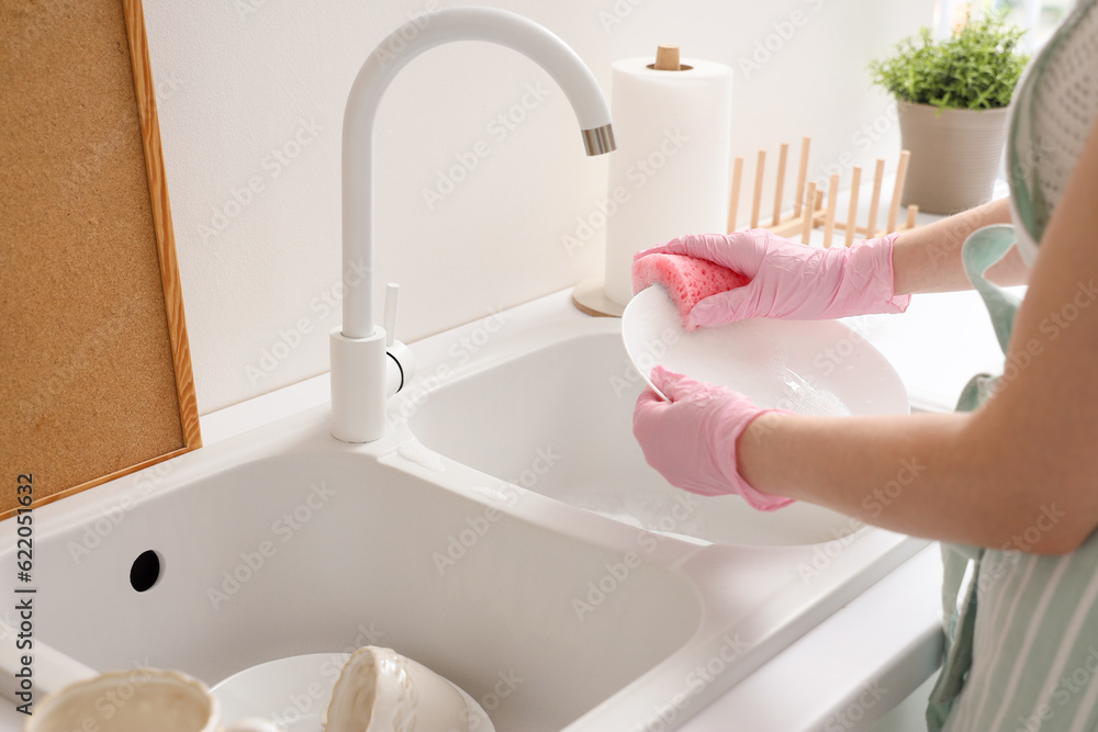 Woman washing plate with sponge in kitchen, closeup