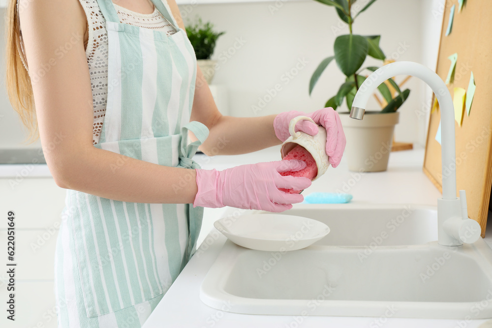 Woman washing cup with sponge in kitchen, closeup