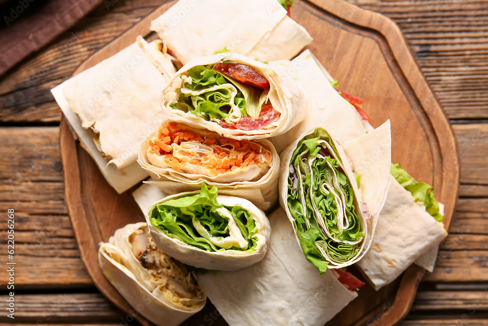 Board of tasty lavash rolls with vegetables and greens on wooden background