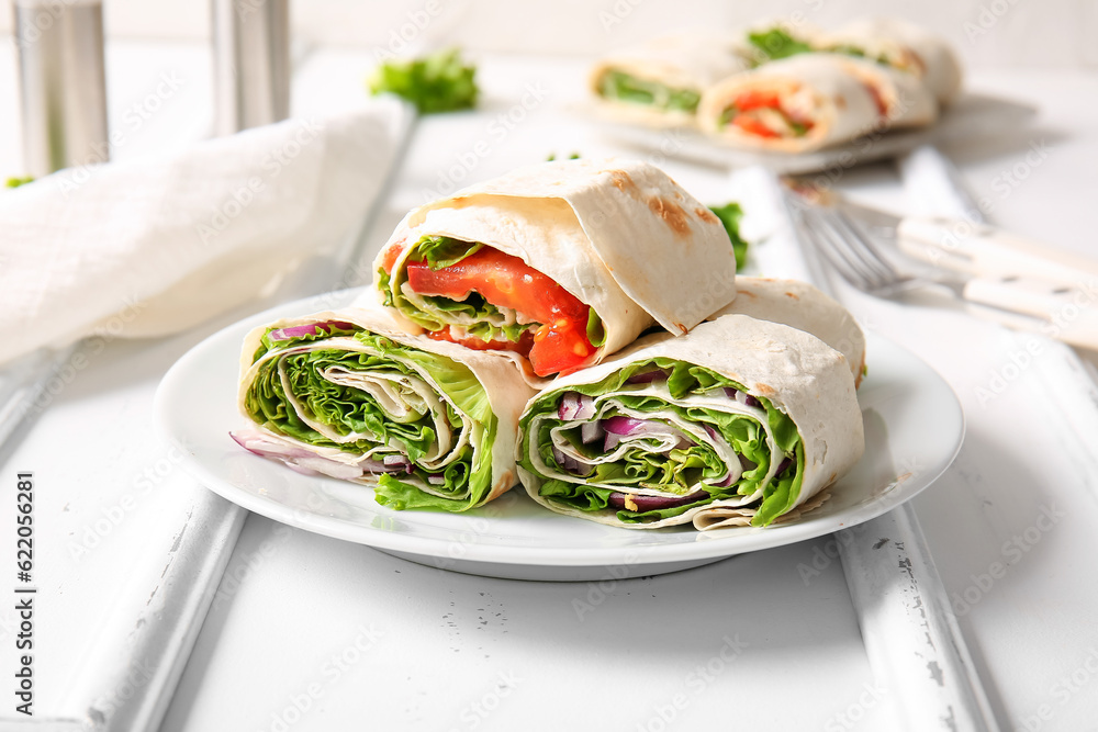 Plate of tasty lavash rolls with vegetables and greens on table