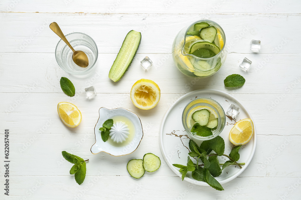Glass and jug of lemonade with cucumber on white background