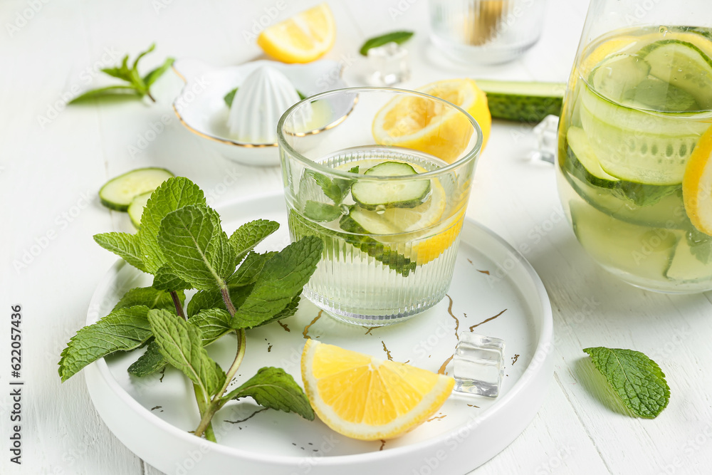 Glass and jug of lemonade with cucumber on white background