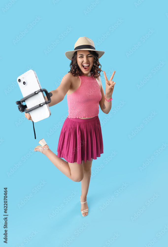 Happy young woman with mobile phone taking selfie on blue background