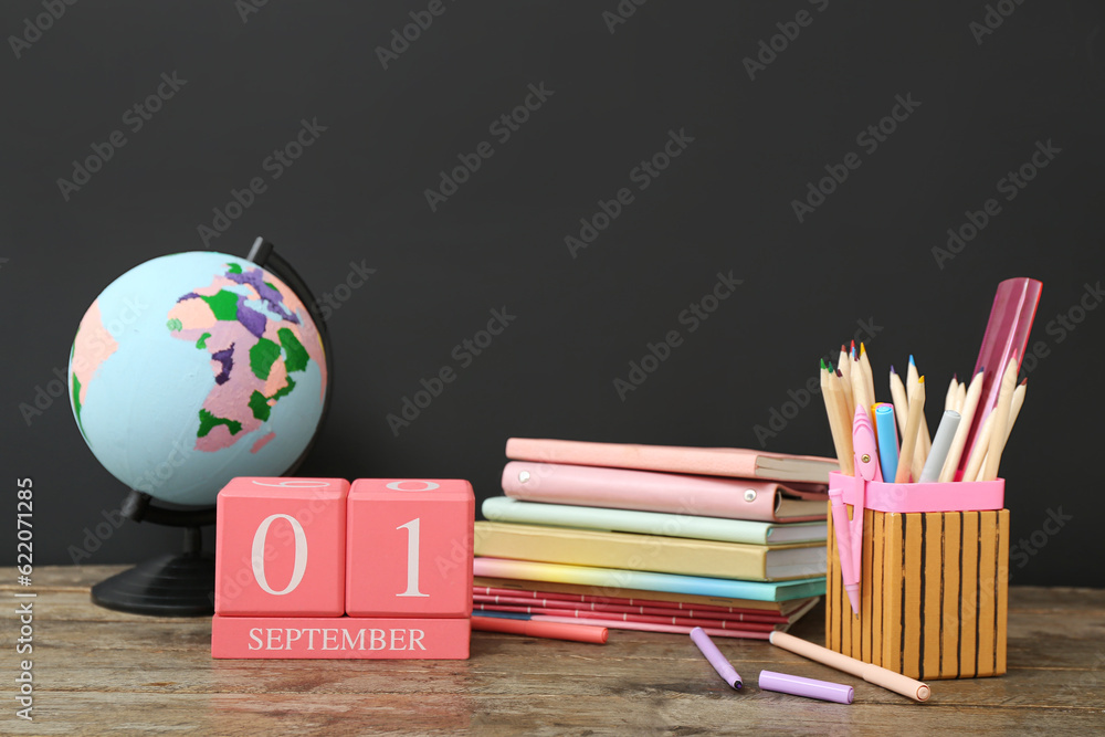 Different stationery, globe and calendar with date SEPTEMBER 1 on wooden table against black chalkbo