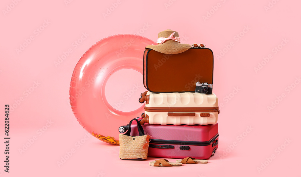 Suitcases with inflatable ring and beach accessories on pink background. Travel concept
