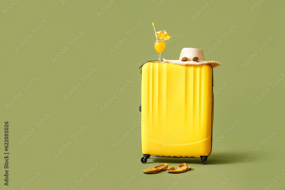 Suitcase with cocktail and beach accessories on green background. Travel concept