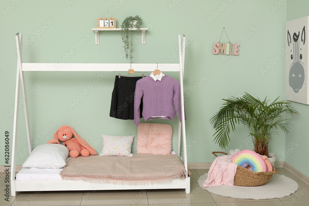 Stylish interior on childrens bedroom with school uniform and houseplant