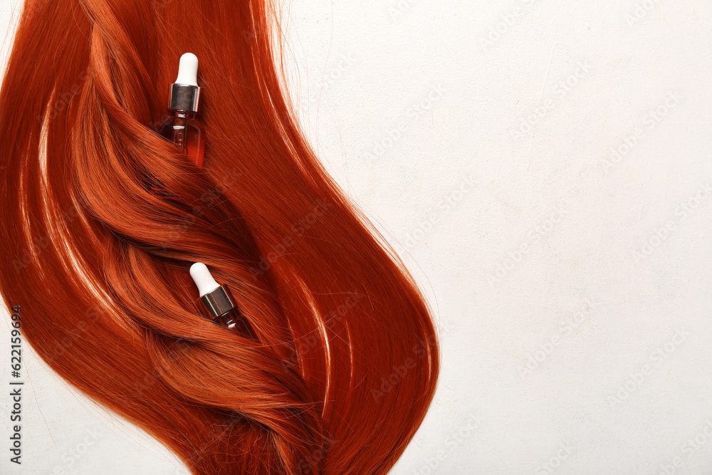Beautiful ginger hair with bottles of essential oil on light background, closeup