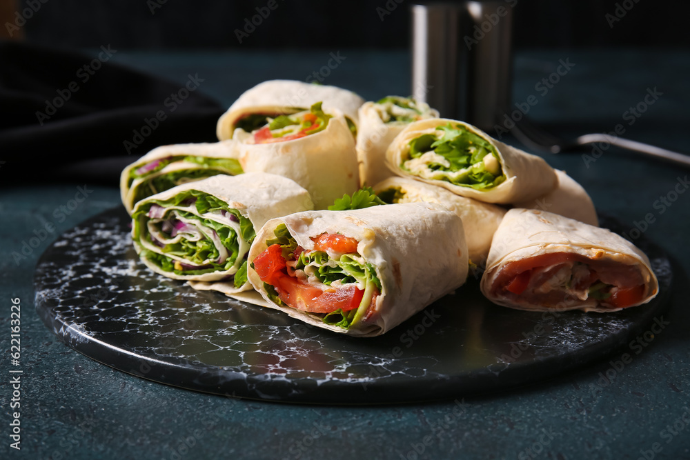 Board of tasty lavash rolls with vegetables and greens on black background