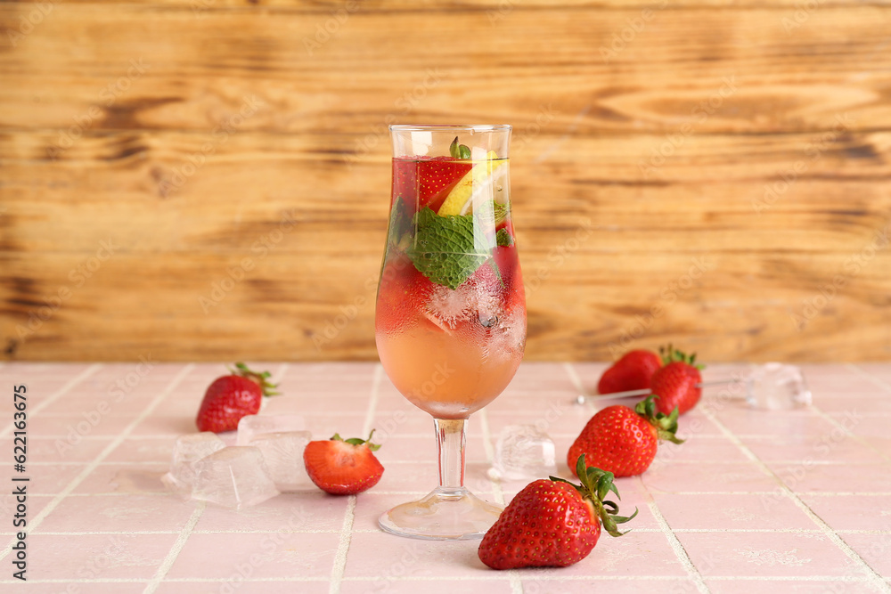 Glass of fresh lemonade with strawberry and lemon on pink tile table