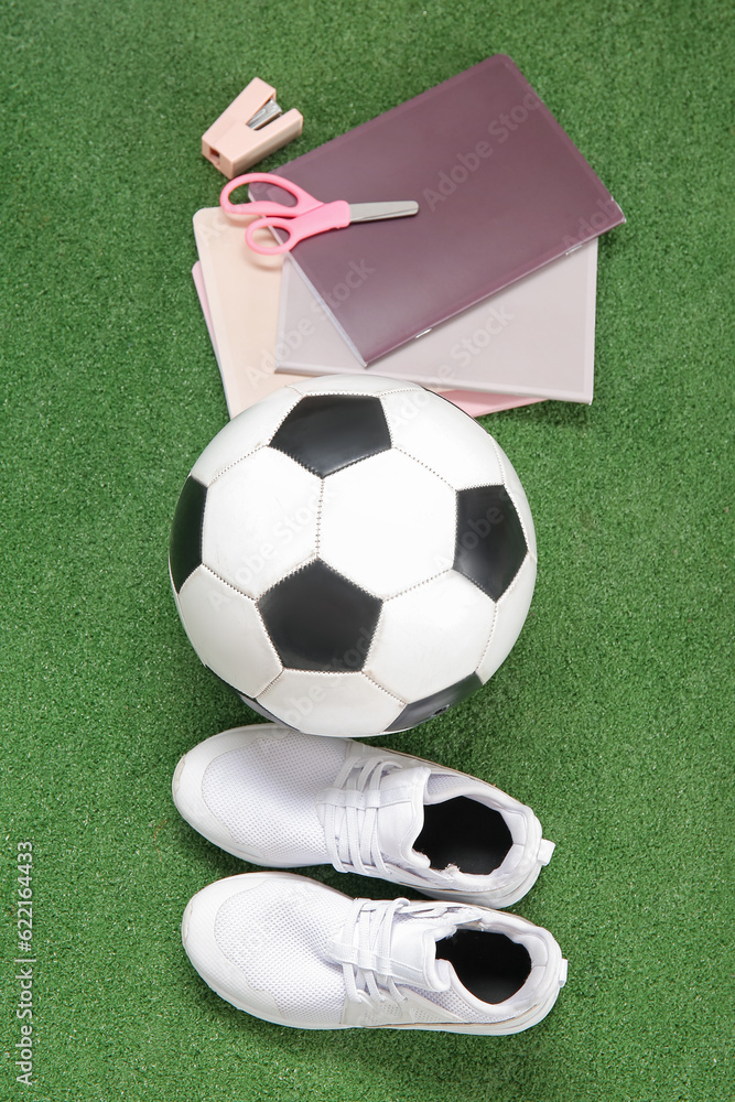Sneakers with soccer ball and different stationery on color background
