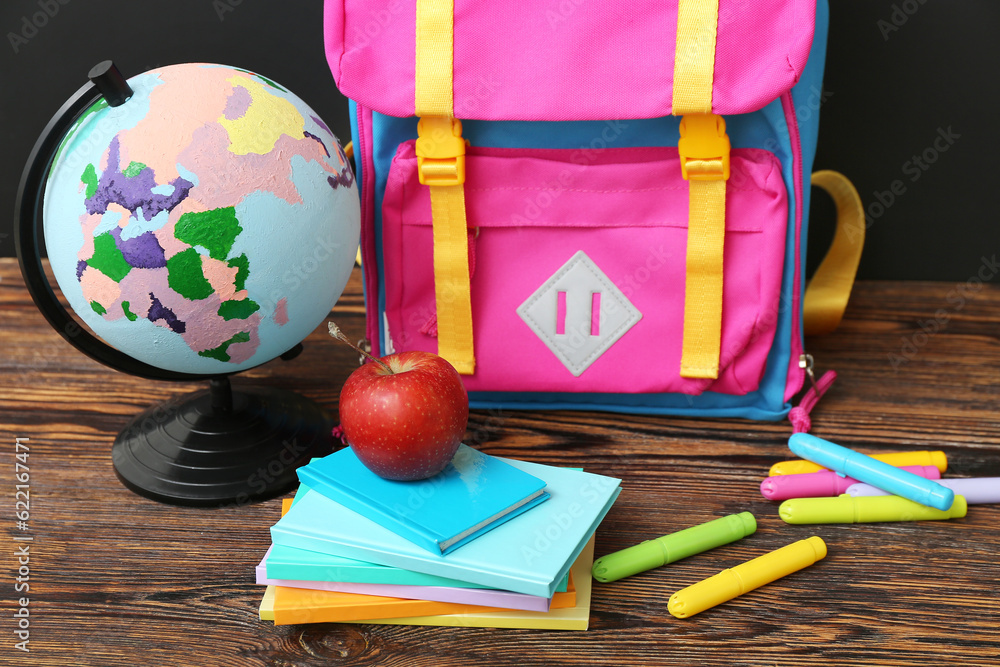Backpack with different stationery and globe on wooden table against black chalkboard