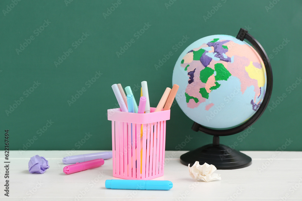 Different stationery with globe on white table against green chalkboard