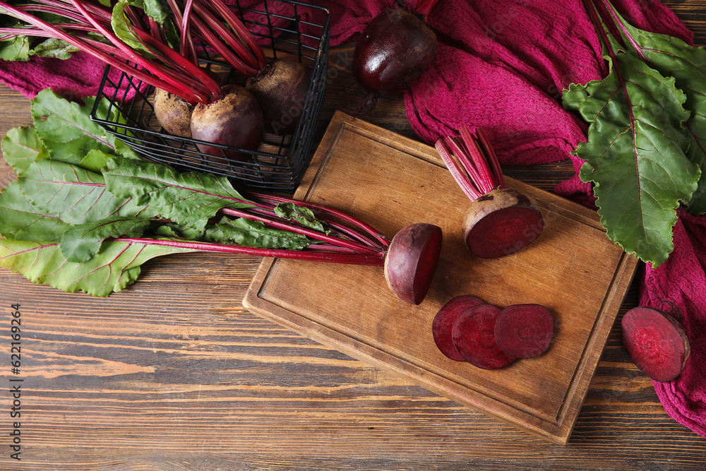 Board and basket of fresh beets with green leaves on wooden background