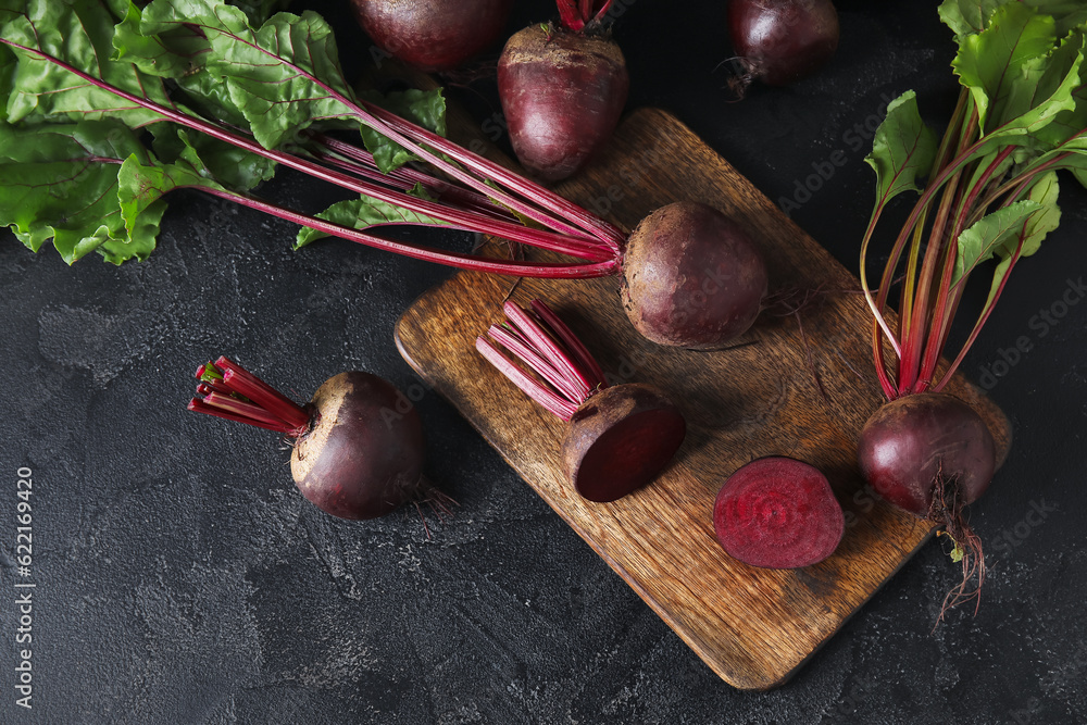 Wooden board of fresh beets with green leaves on black background