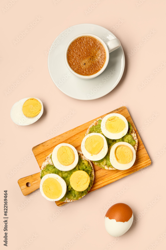 Wooden board of rice crackers with boiled eggs and avocado on pink background