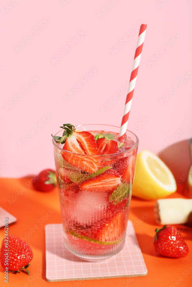 Glass of fresh strawberry mojito with straw and ingredients on orange table near pink wall