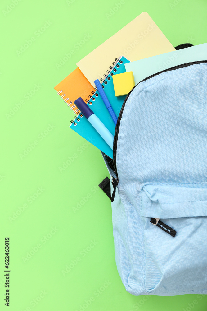 Blue school backpack with notebooks and markers on green background