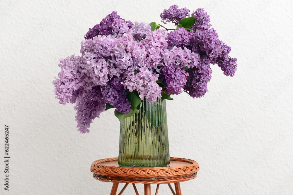 Vase with beautiful lilac flowers on table near white wall in room, closeup