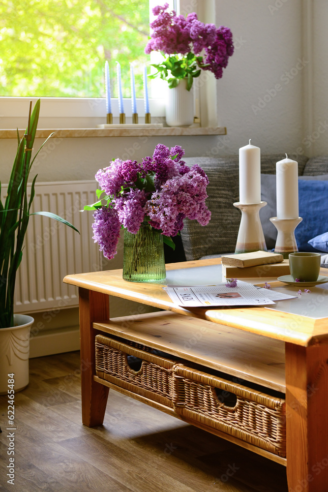 Vase with beautiful lilac flowers and candles on table in interior of light living room