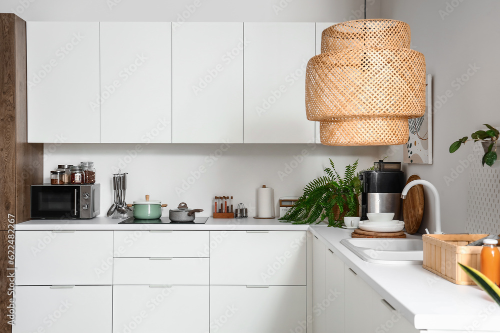 Interior of light kitchen with white counters, cupboards and lamp