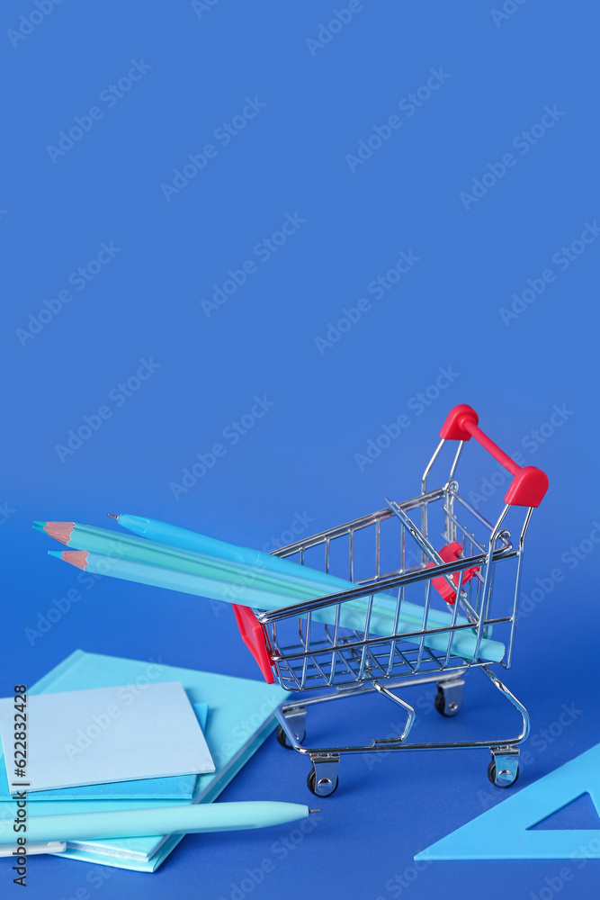Shopping cart with stationery on blue background