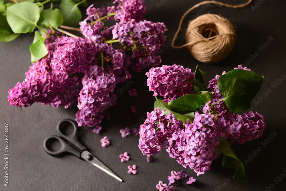 Beautiful lilac flowers with scissors and threads on dark background