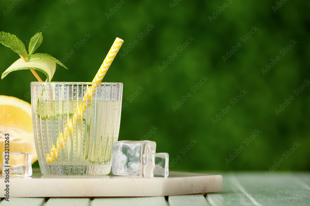 Glass of lemonade with cucumber and mint on green wooden table outdoors