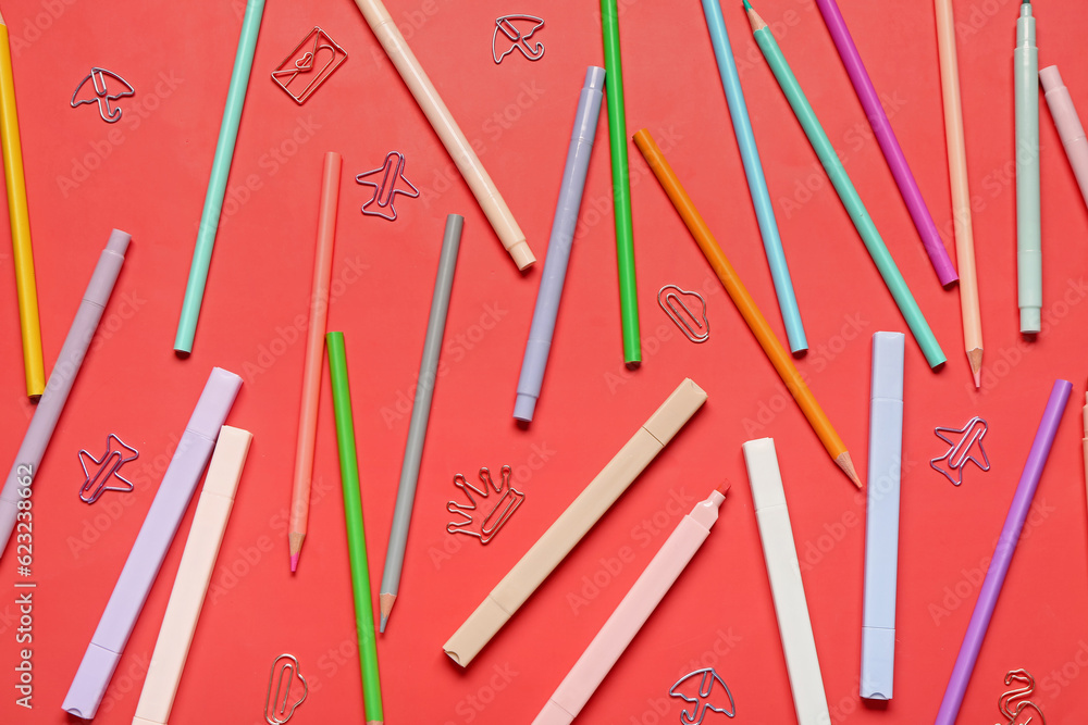 Colorful pencils and markers with paper clips in different shapes on red background