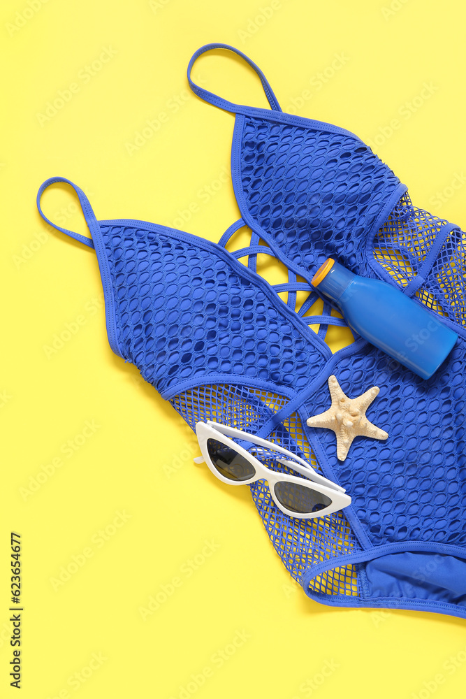 Stylish swimsuit, sunglasses and bottle of sunscreen cream on yellow background