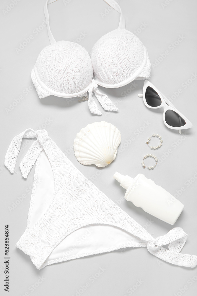 Stylish swimsuit, sunglasses, bottle of sunscreen cream, earrings and seashell on light background