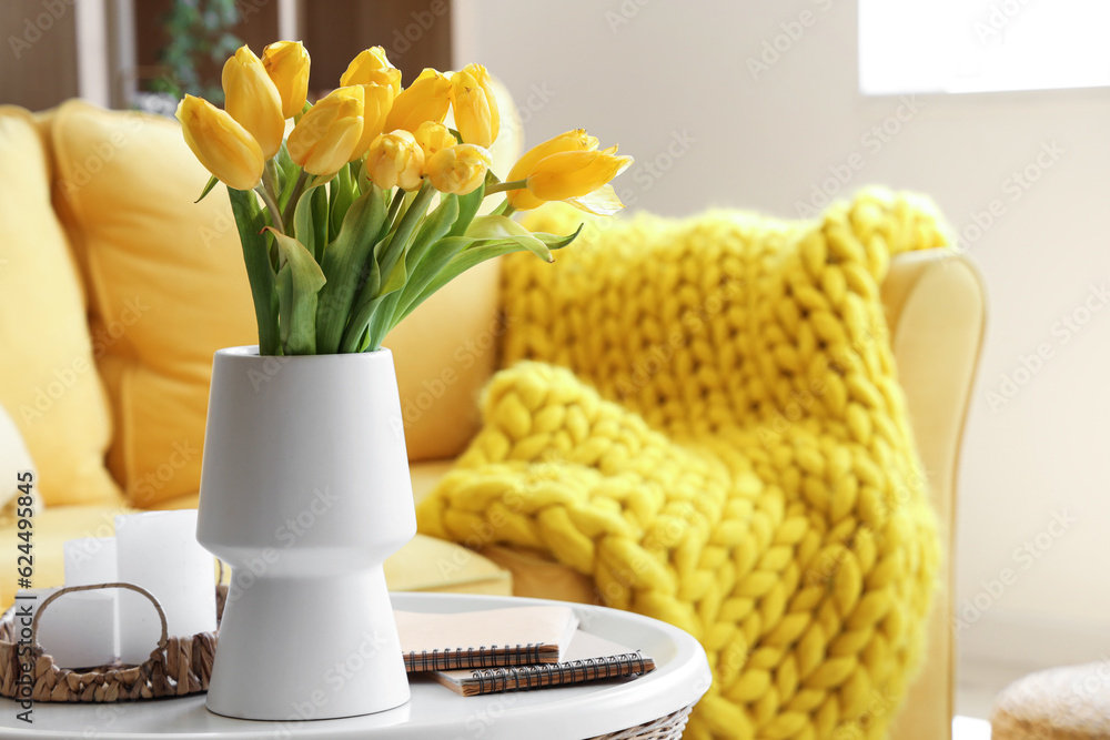 Vase with blooming tulip flowers on coffee table in interior of living room
