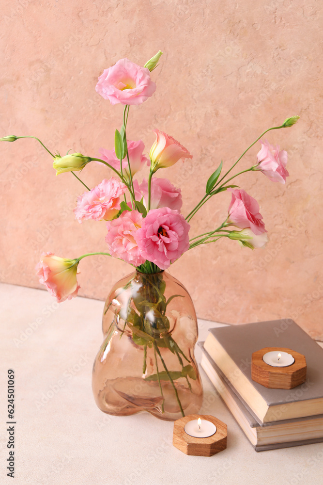 Vase with beautiful pink eustoma flowers, books and candles on light table