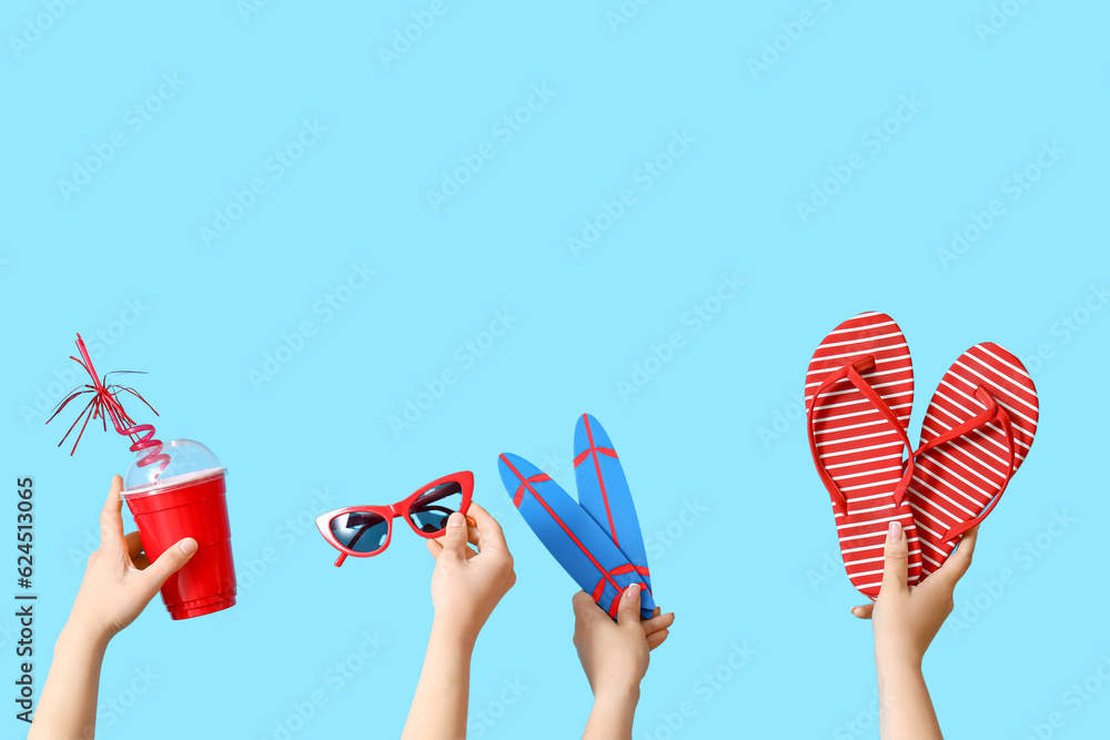 Female hands with beach accessories, mini surfboards and cup on blue background