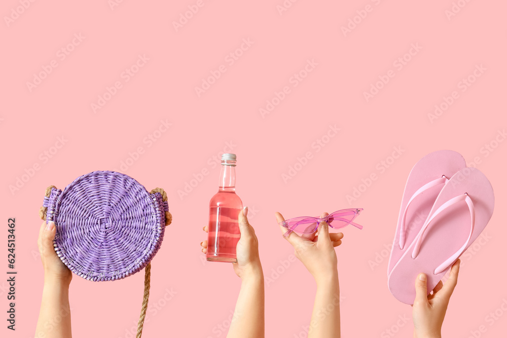Many hands with beach accessories and bottle of cocktail on pink background