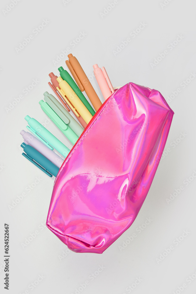 Colorful pens in pink pencil case on grey background