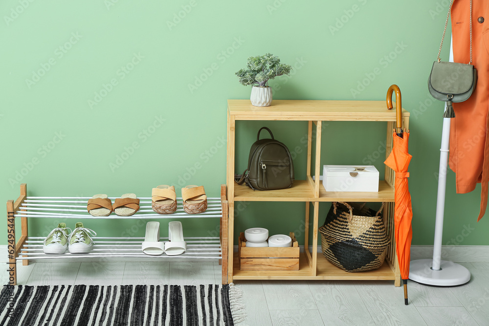 Shelving unit and stand with shoes near green wall in hall