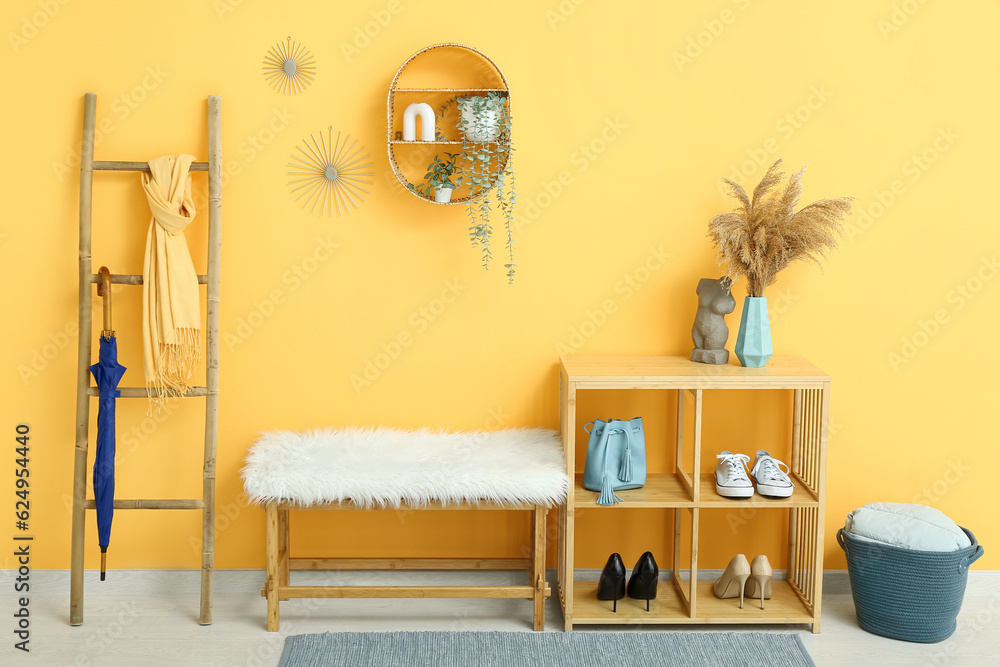 Shelving unit with shoes, bench, shelf and ladder near orange wall in hall