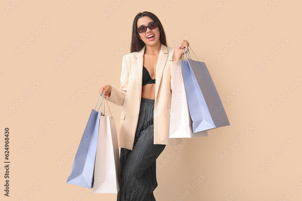 Happy beautiful young woman with shopping bags on beige background