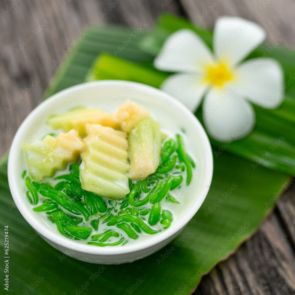 Appetizing lod chong placed on a green banana leaf decorated with white champa flowers on a wooden t