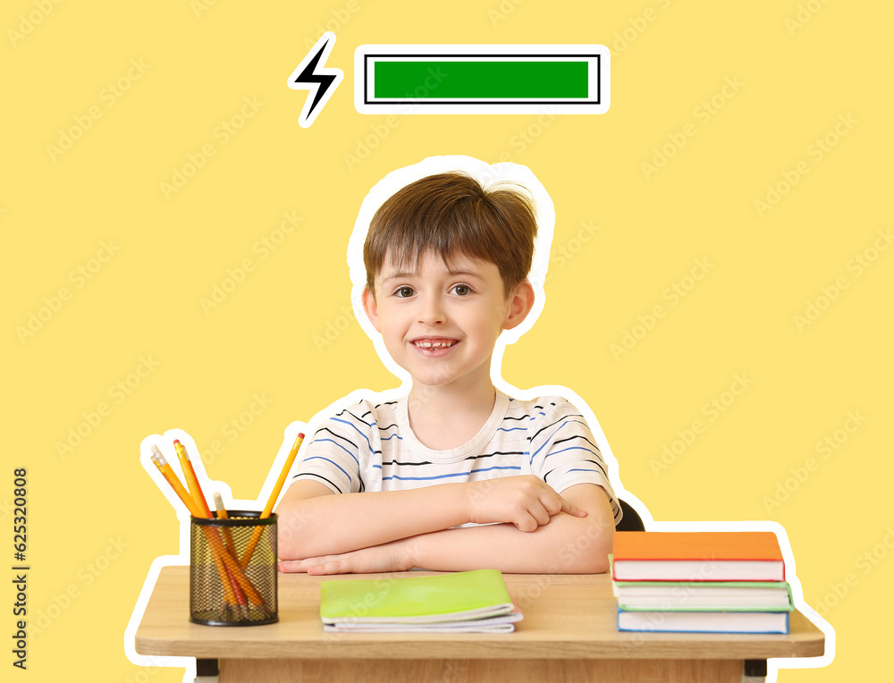 Smart little boy sitting at desk against yellow background