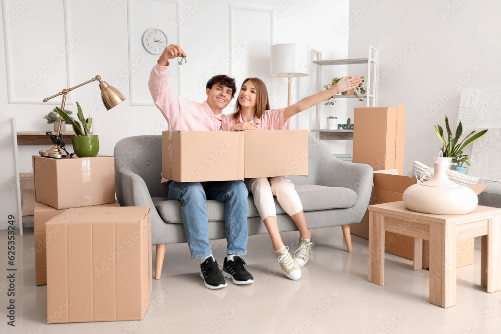 Young couple with keys and moving boxes in their new flat